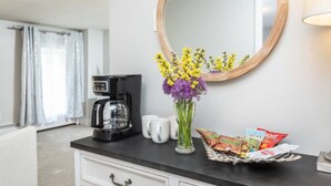 A kitchen counter with a coffee maker, a vase with flowers, and a basket of snacks. - The Sugar Maple - Suite (Harrisonburg)
