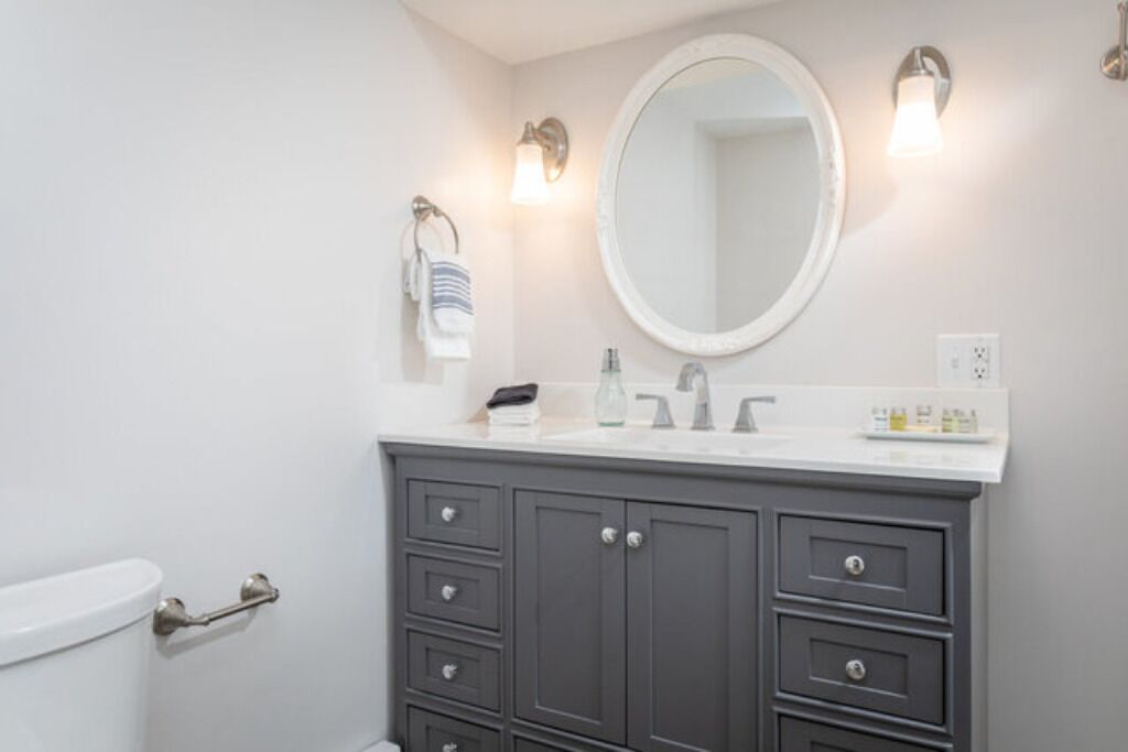 A bathroom with a white toilet, a gray vanity with a mirror, and two wall-mounted light fixtures.