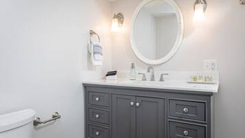 A bathroom with a white toilet, a gray vanity with a mirror, and two wall-mounted light fixtures.