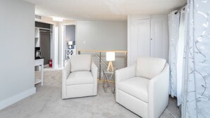 A room with two white armchairs, a small table, a lamp, and a closet. - The Sugar Maple - Suite (Harrisonburg)