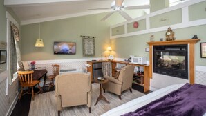 Une chambre d’hôtel comprenant un lit, un bureau avec une chaise, une petite table, une cheminée et un téléviseur fixé au mur.