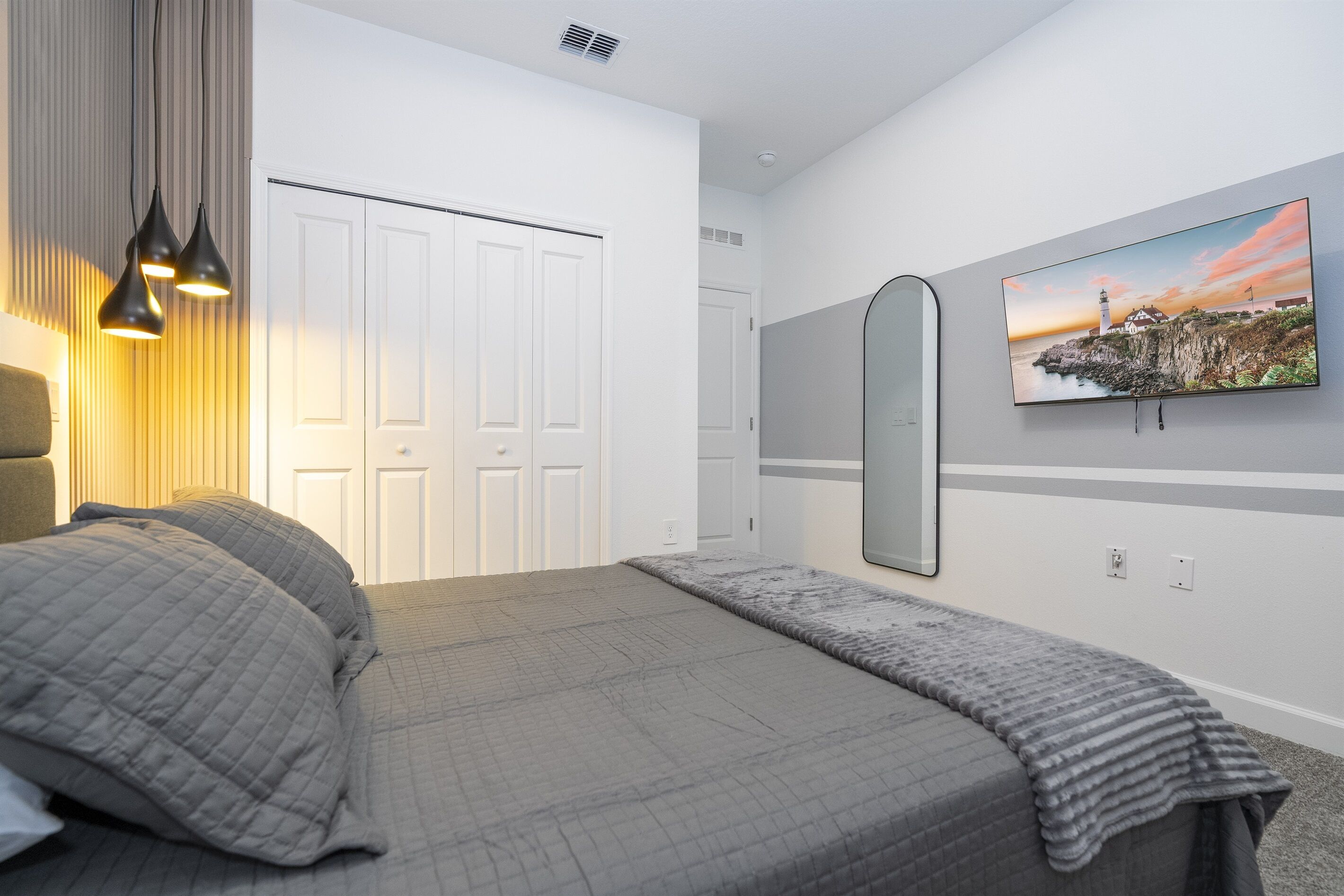 Una camera da letto con un letto, una TV a muro e una porta con uno specchio.