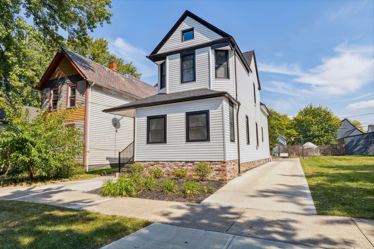 A two-story house with a brick foundation, a front porch, and a driveway.
