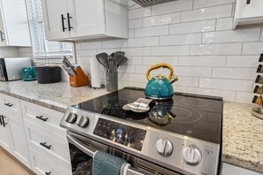 A modern kitchen with a stainless steel stove, a teal kettle, and white cabinets.
