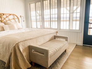 Ein Schlafzimmer mit einem großen Bett, einer Bank und Blick ins Freie durch große Fenster.