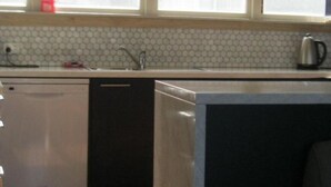 Uma cozinha com janela, pia e chaleira no balcão.