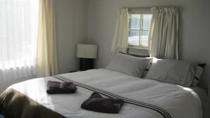 Quarto de hotel com cama, mesa de cabeceira, luminária e janela com cortinas.