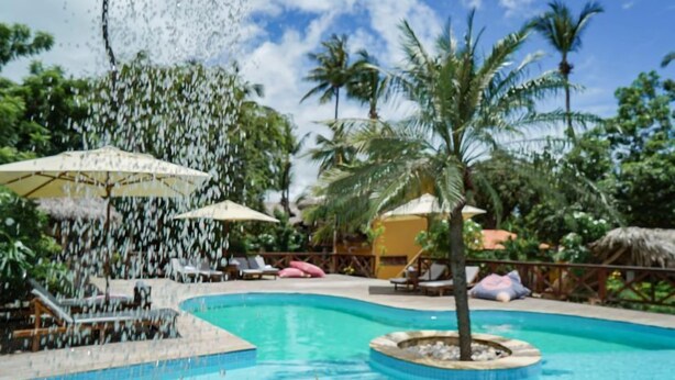 A pool area with lounge chairs and umbrellas, surrounded by palm trees and a clear sky. - Pousada Rota dos Ventos (Cajueiro da Praia)
