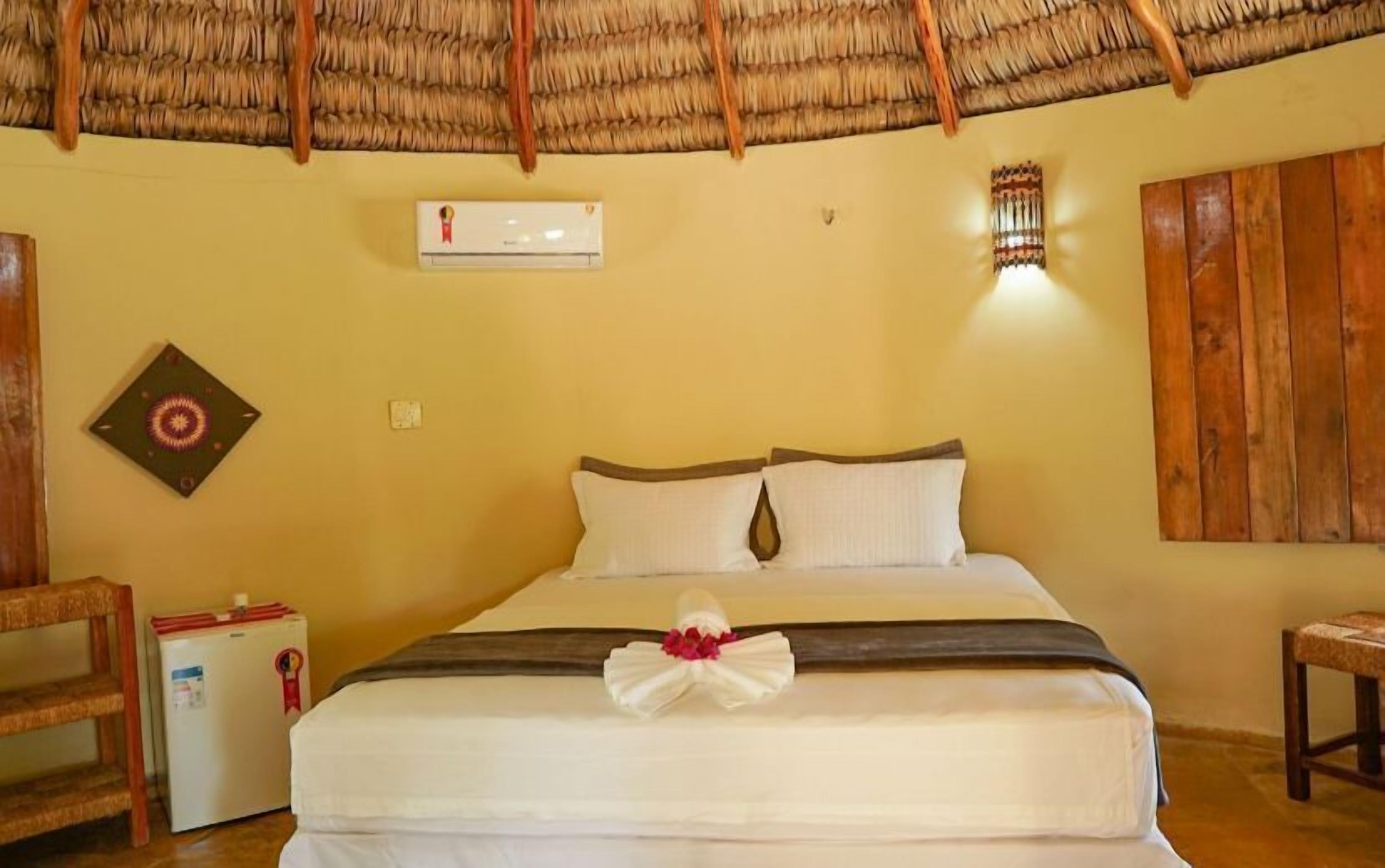 Habitación de hotel con cama, un refrigerador pequeño, aire acondicionado instalado en la pared y techo tejido.