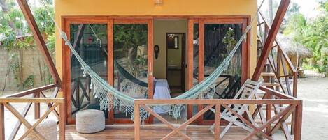 A wooden deck with a hammock, a small round seating area, and a door leading to an interior space.