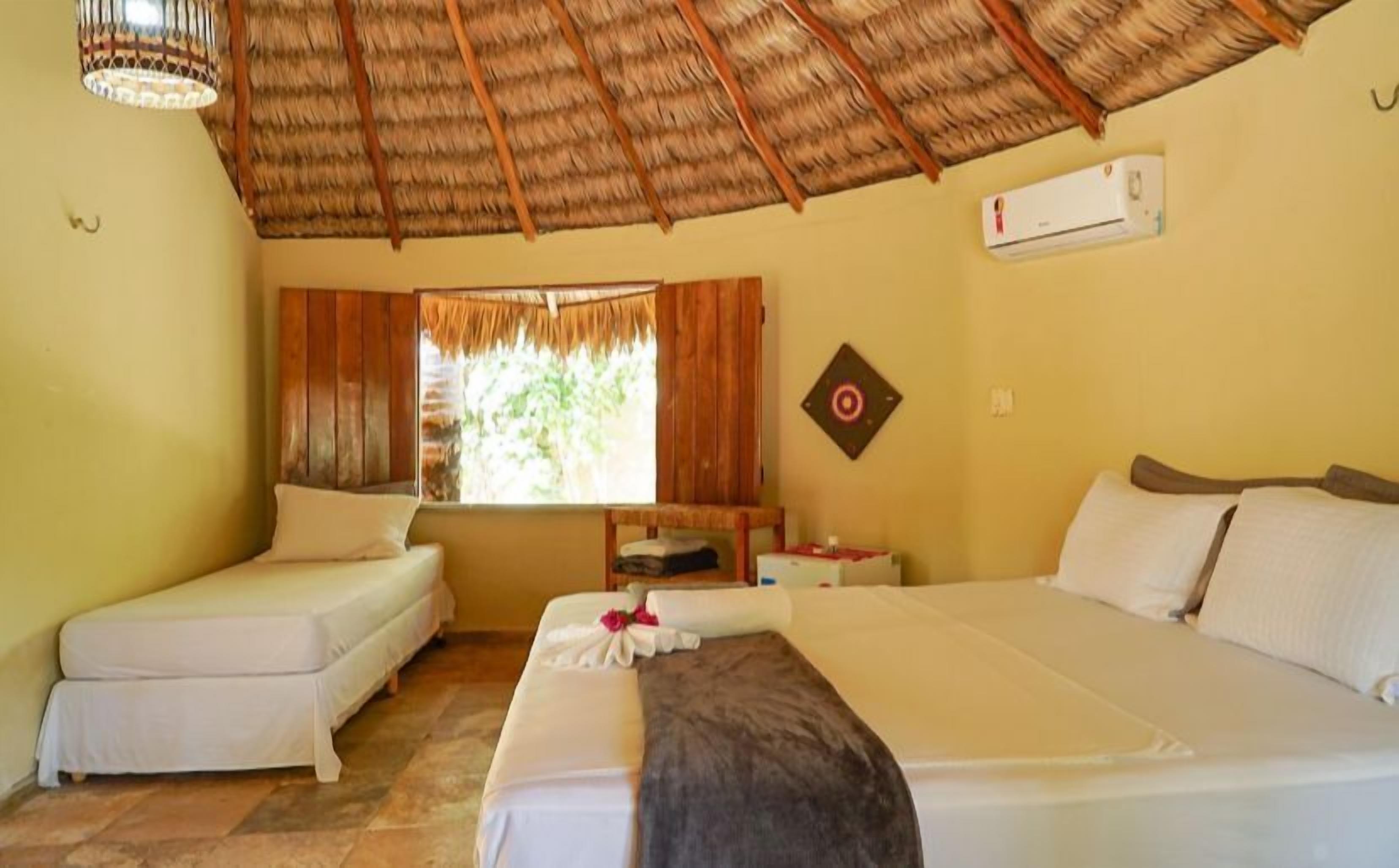 A room with two beds, a window with curtains, a ceiling fan, and a wall-mounted air conditioner.