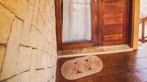 A wooden door with a glass panel, a woven wall hanging, and a stone wall. - Pousada Rota dos Ventos (Cajueiro da Praia)