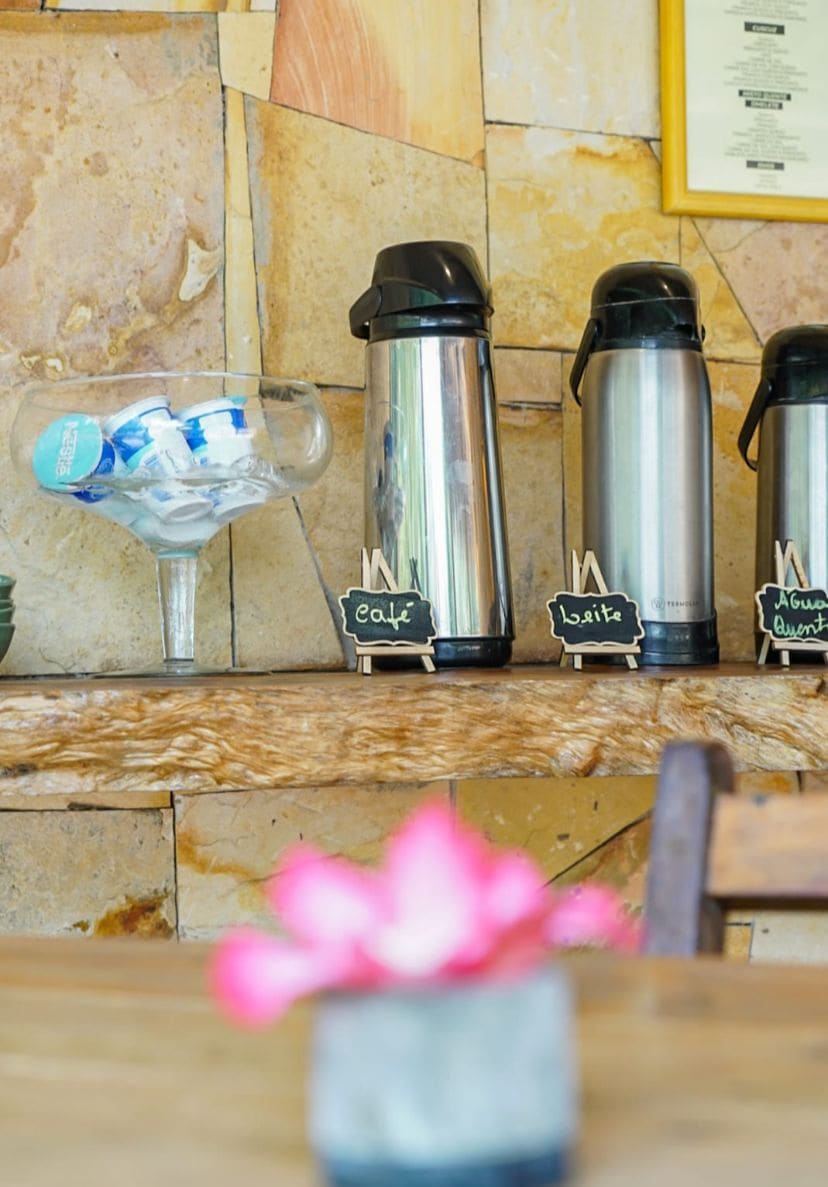A coffee station with three stainless steel thermos cups labeled 'cafe,' 'leite,' and 'aguarela.'