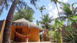 A thatched-roof hut with a hammock, surrounded by palm trees and tropical vegetation. - Pousada Rota dos Ventos (Cajueiro da Praia)