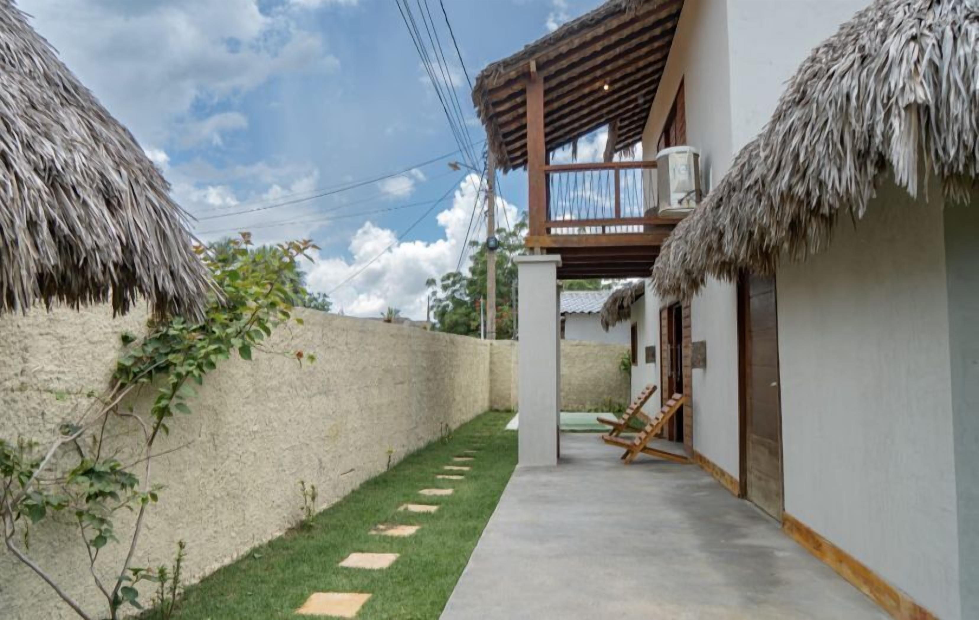 A modern house with a thatched roof, a concrete pathway, and a wooden deck with chairs.