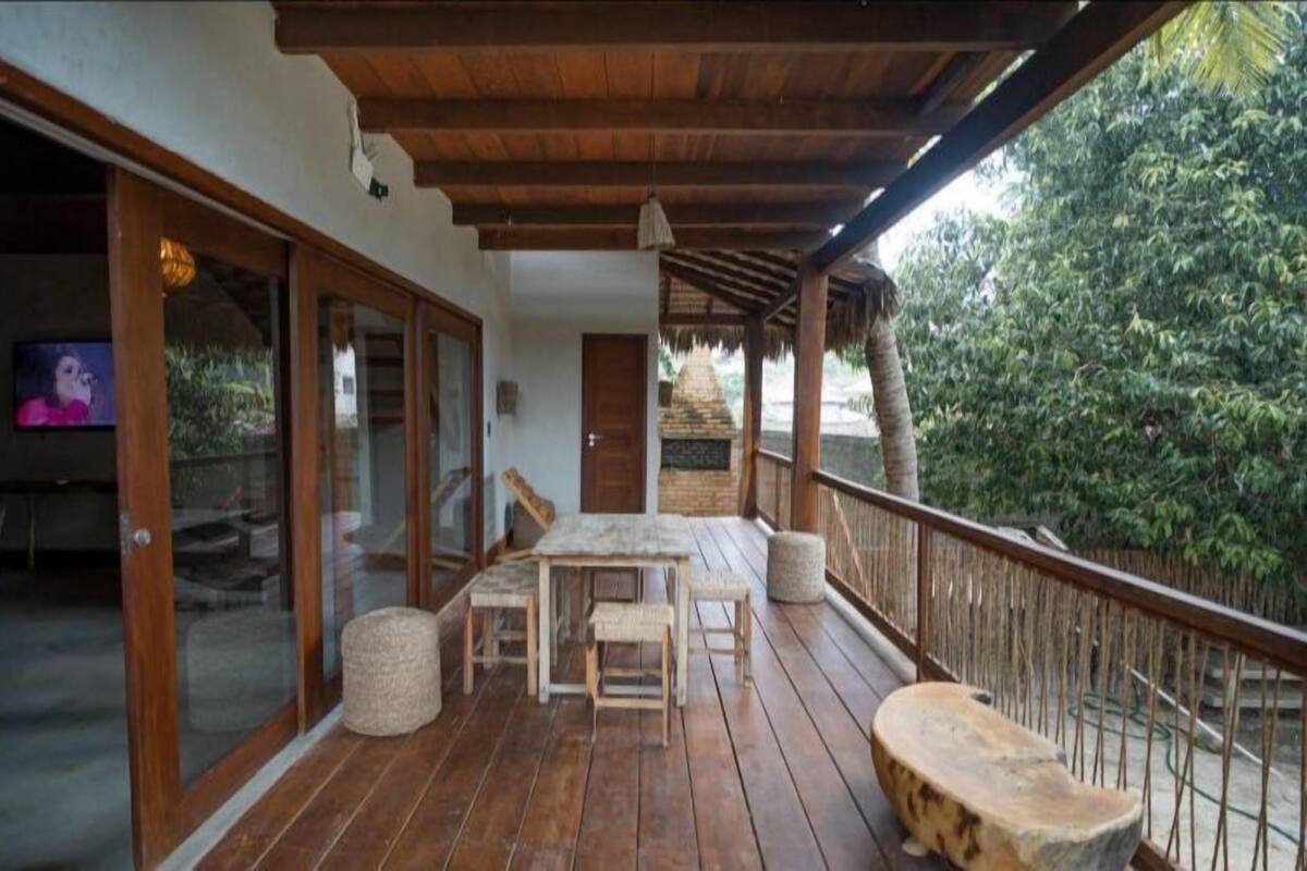 A wooden deck with a table and chairs, a TV, and a thatched-roof structure.