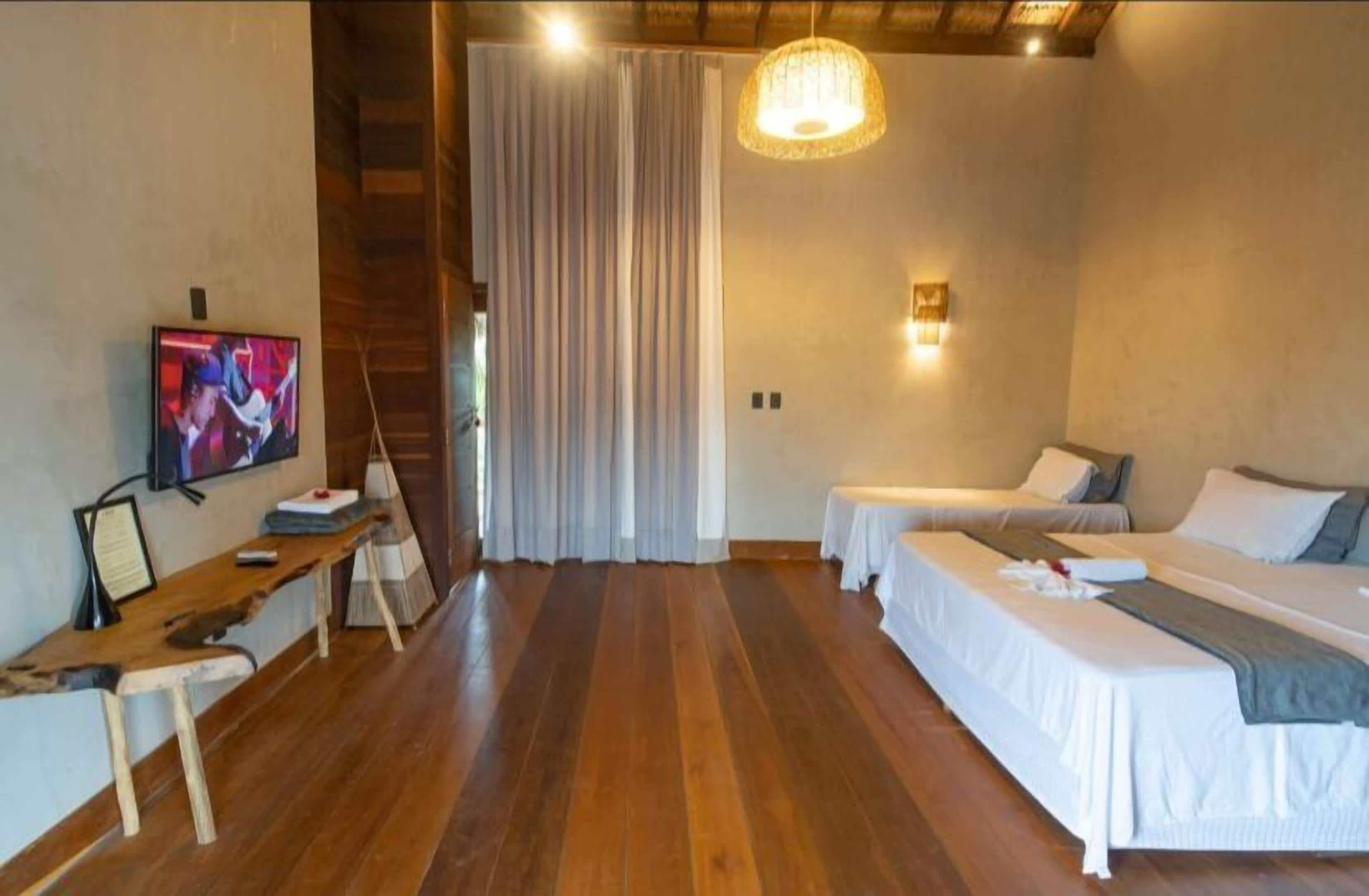 A room with wooden flooring, two beds, a desk with a chair, a television, and a staircase.