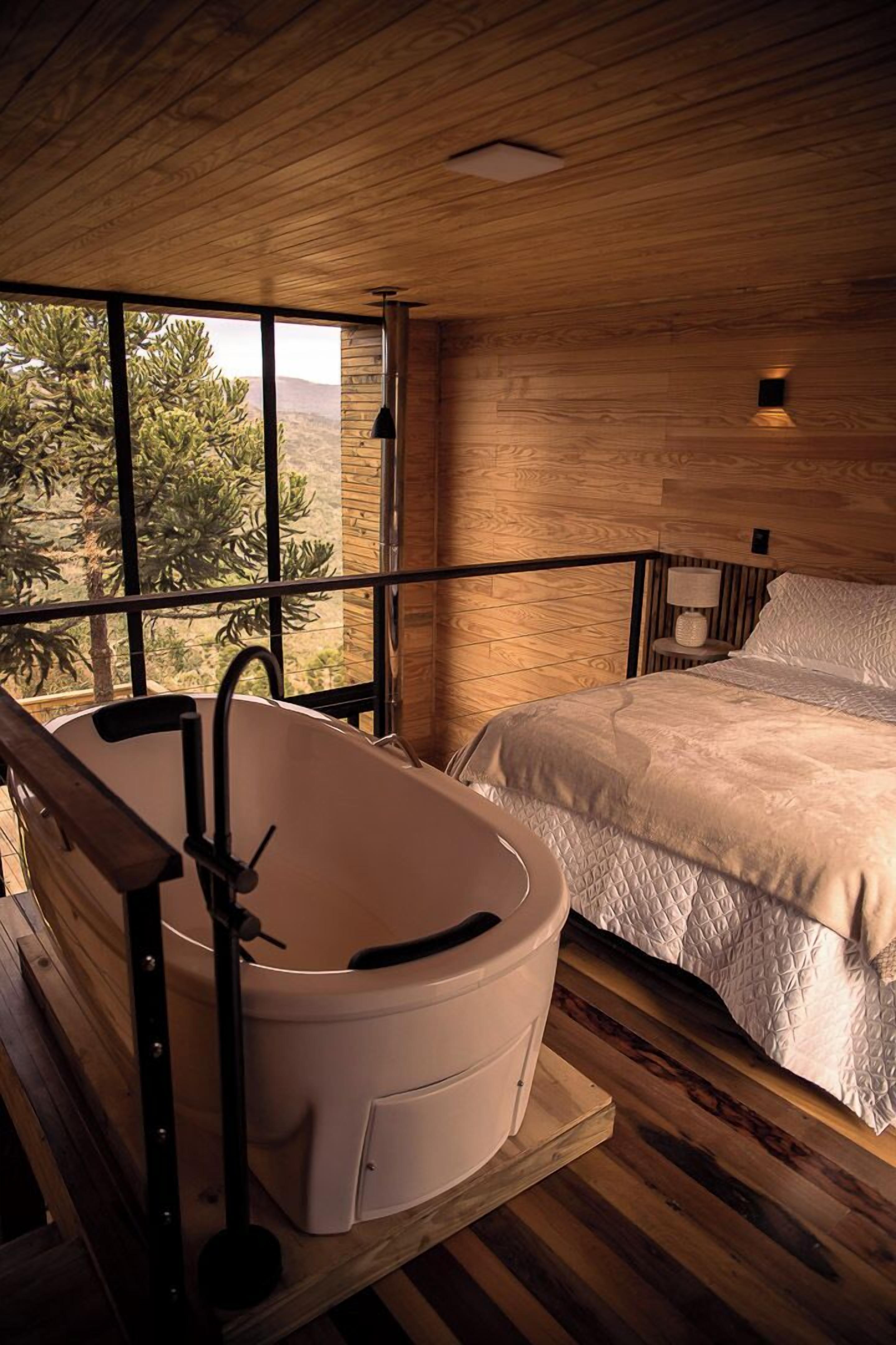 Un dormitorio con un ventanal grande, una bañera blanca y una cama con cubrecama blanco.