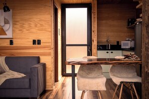 A compact living space with a wooden interior, a sofa, a dining table with two chairs, and a kitchen area with a microwave. - Rancho Denver (Urubici)