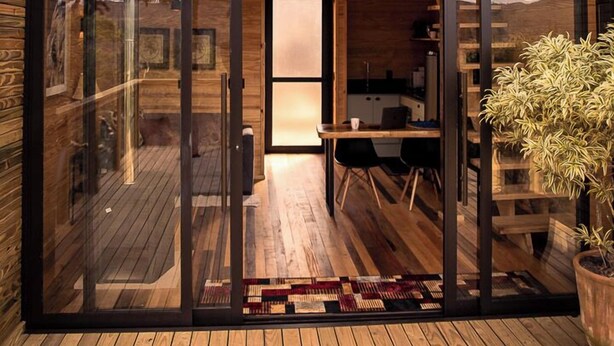 A modern two-story building with large glass windows, a wooden deck, and a dining area with a table and chairs. - Rancho Denver (Urubici)