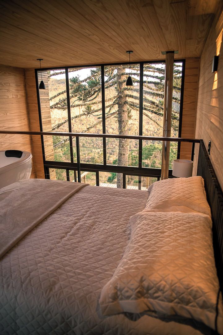 A bedroom with a large window, wooden walls, and a bed with a quilted mattress.