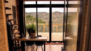 A wooden interior with a dining area, a potted plant, and a view of a deck and mountains. - Rancho Denver (Urubici)