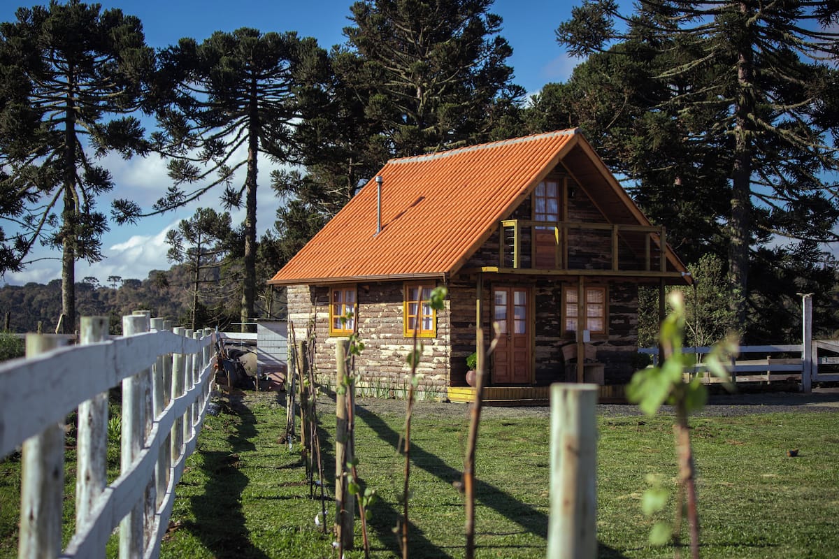 A log cabin with a sloped roof, wooden windows, and a stone foundation.