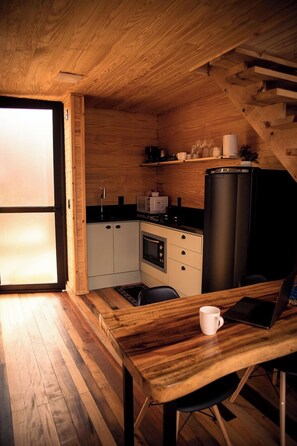 A compact kitchen with wooden cabinetry, a black refrigerator, and a dining area with a wooden table and chairs.