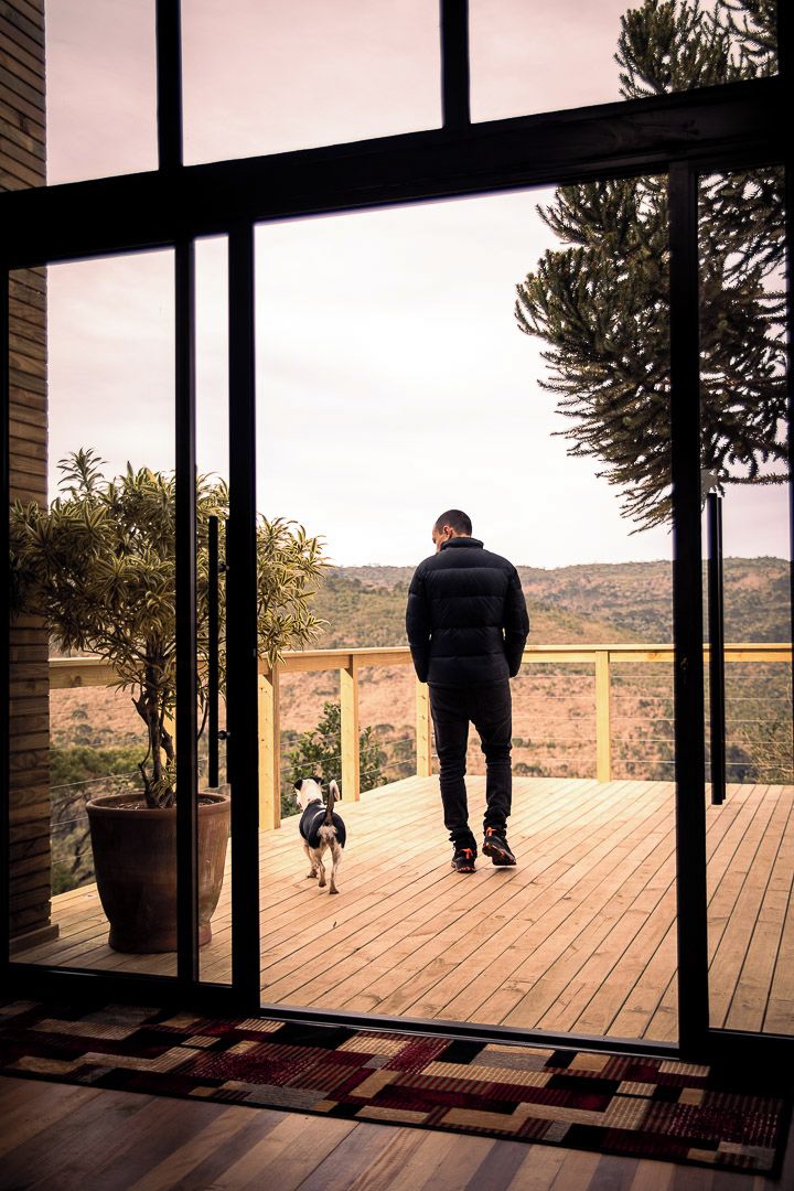 Un hombre está de pie en una terraza de madera con vistas a un paisaje montañoso.