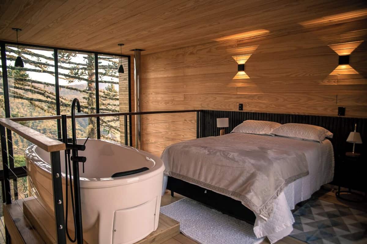 A bedroom with a large bed, a bathtub, and a view of the outdoors.