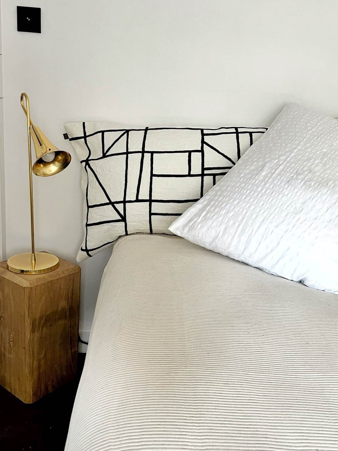A bed with a textured white cover, a geometric-patterned headboard, and a gold floor lamp on a wooden nightstand.