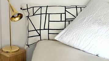 A bed with a textured white cover, a geometric-patterned headboard, and a gold floor lamp on a wooden nightstand.