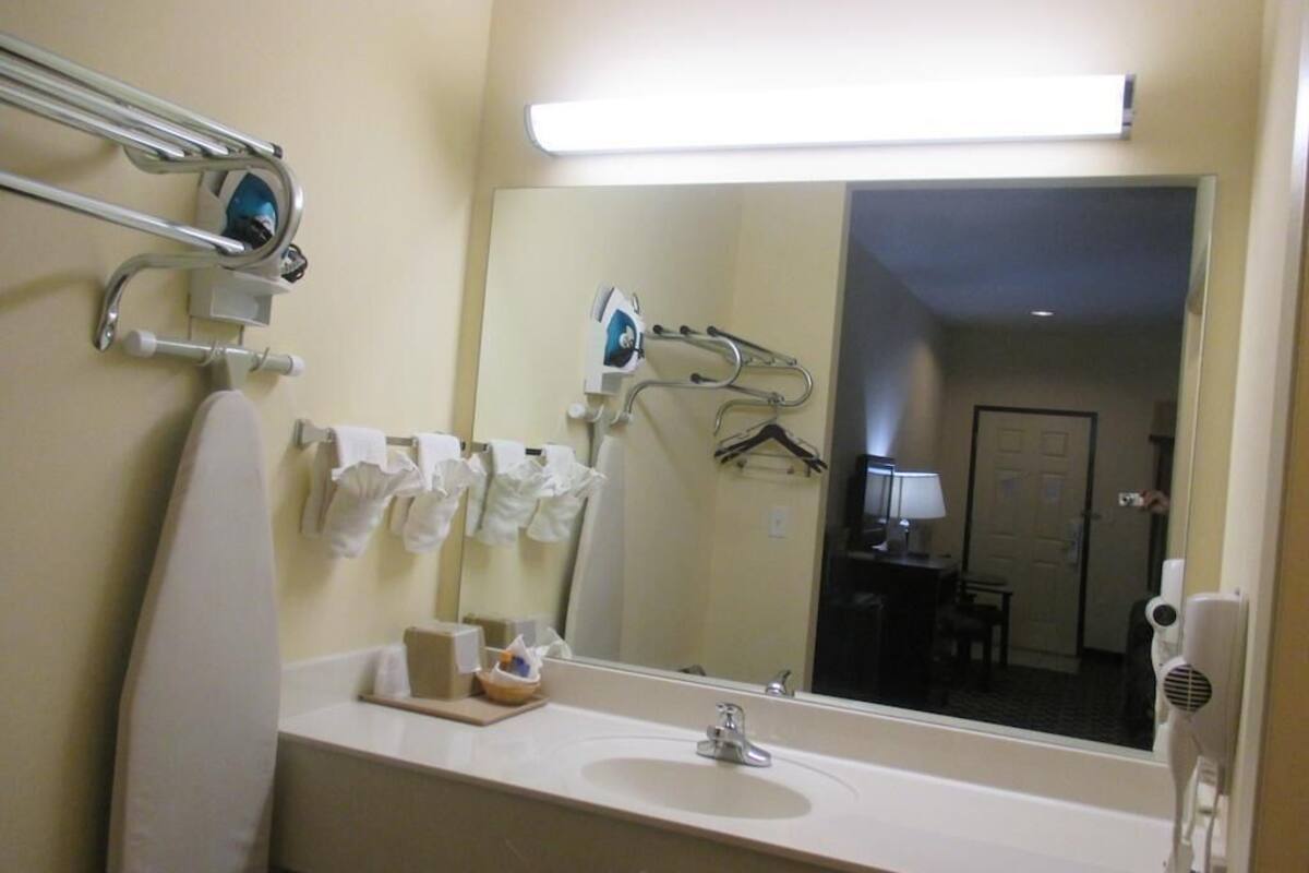 A hotel bathroom with a large mirror, a sink, a towel rack, and a hairdryer.
