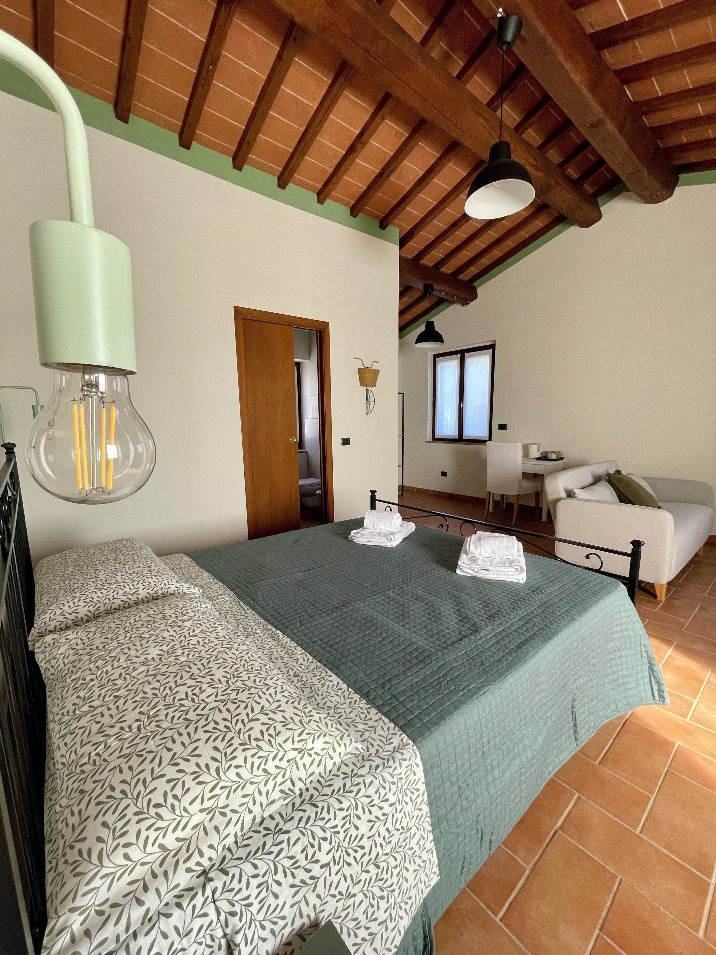 Un dormitorio con cama, escritorio, silla, ventana y techo de madera.