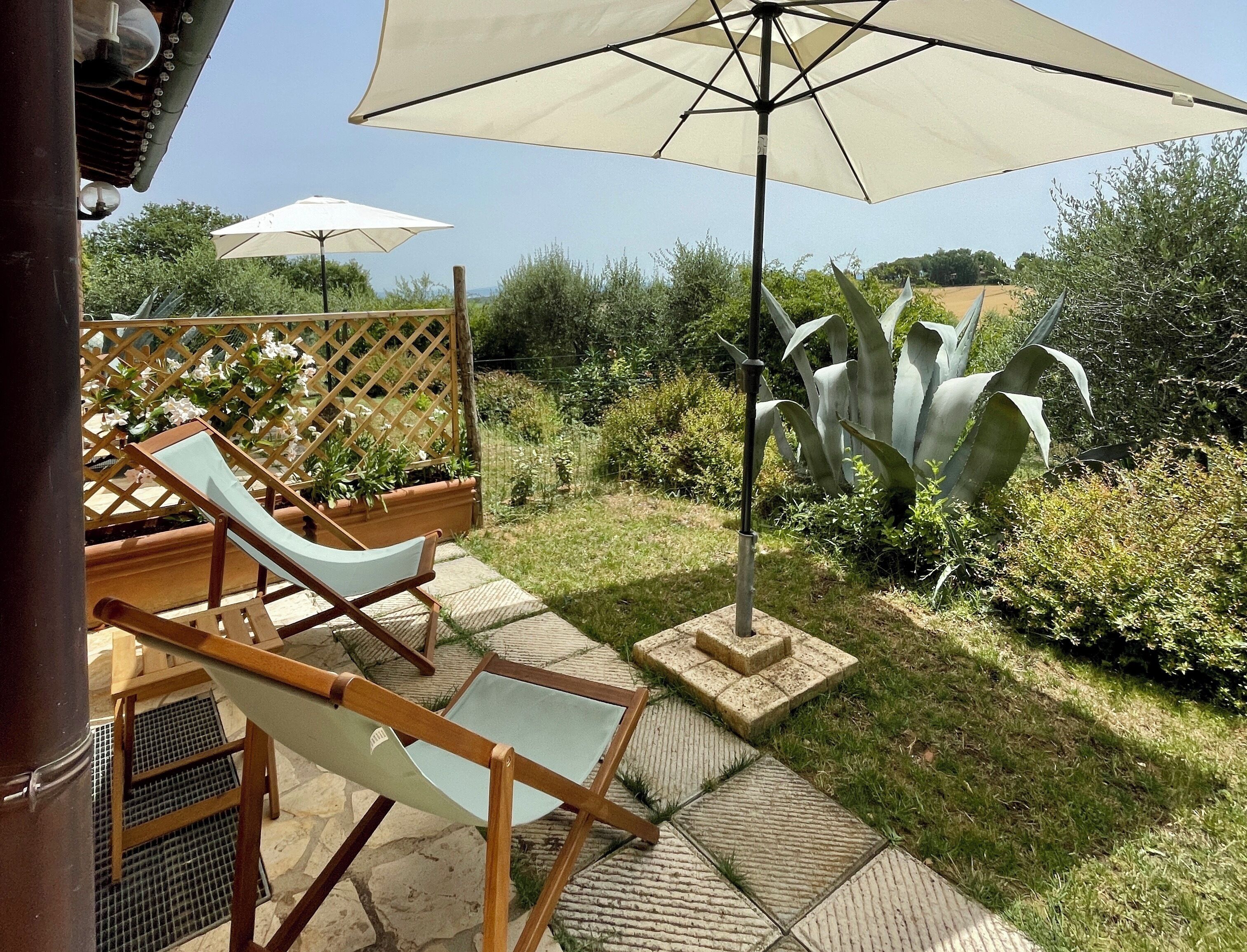 A patio with two lounge chairs, a wooden table, and a large umbrella.