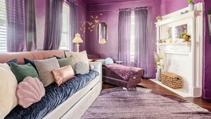 A room with a purple wall, a white fireplace, a sofa with cushions, and a mirror on the wall.