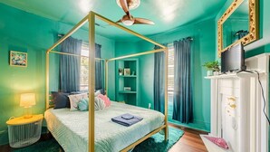 A four-poster bed with a ceiling fan, a white dresser, and a television on a white mantelpiece.