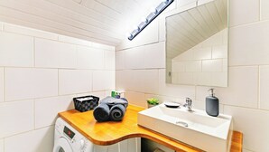 A compact bathroom with a washing machine, a wooden countertop, a sink with a soap dispenser, and a mirror. - Cosy air-conditioned studio with secure parking (Lyon)