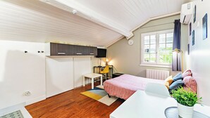 A compact room with a bed, a desk, a chair, a small table, a potted plant, and a window with curtains. - Cosy air-conditioned studio with secure parking (Lyon)