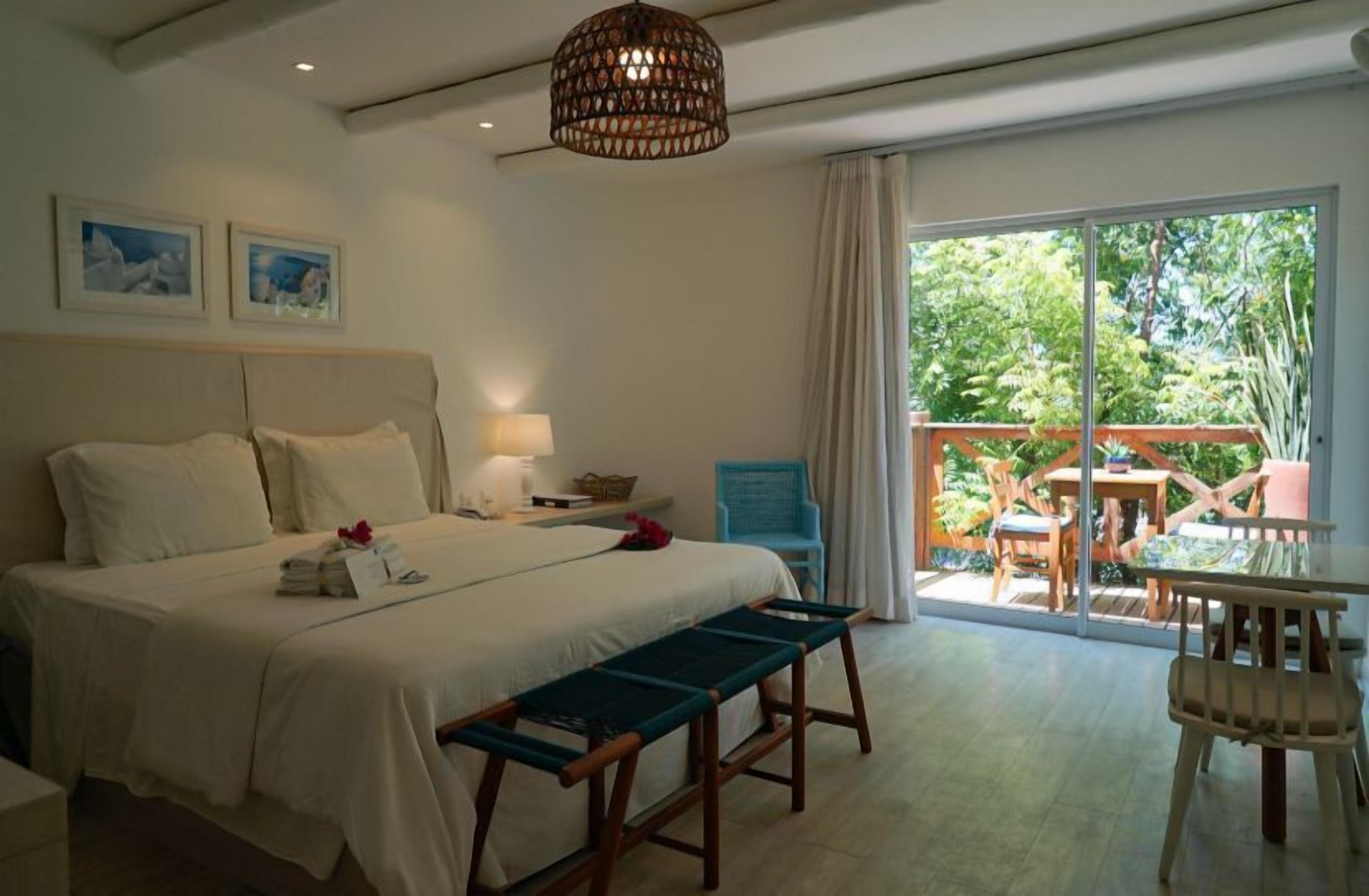Habitación de hotel con cama, banca, mesa, silla y vistas al exterior.