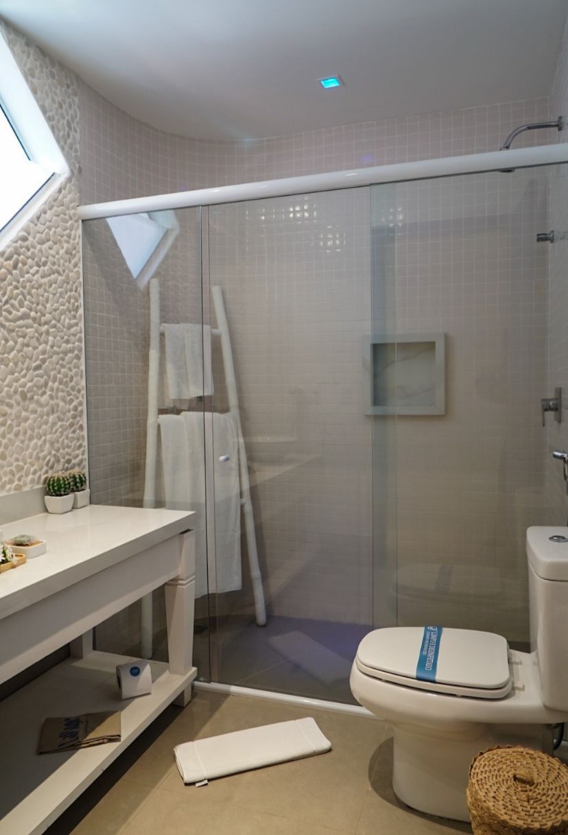 A modern bathroom with a glass shower enclosure, a toilet with a blue label, a white sink with a small plant, and a textured wall.