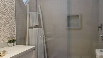 A modern bathroom with a glass shower enclosure, a toilet with a blue label, a white sink with a small plant, and a textured wall.