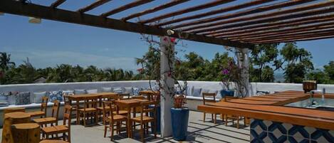 An outdoor patio with wooden furniture, a bar area, and a view of the ocean.