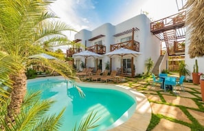 Un moderno resort con piscina, mobiliario exterior y una estructura de techo de paja.