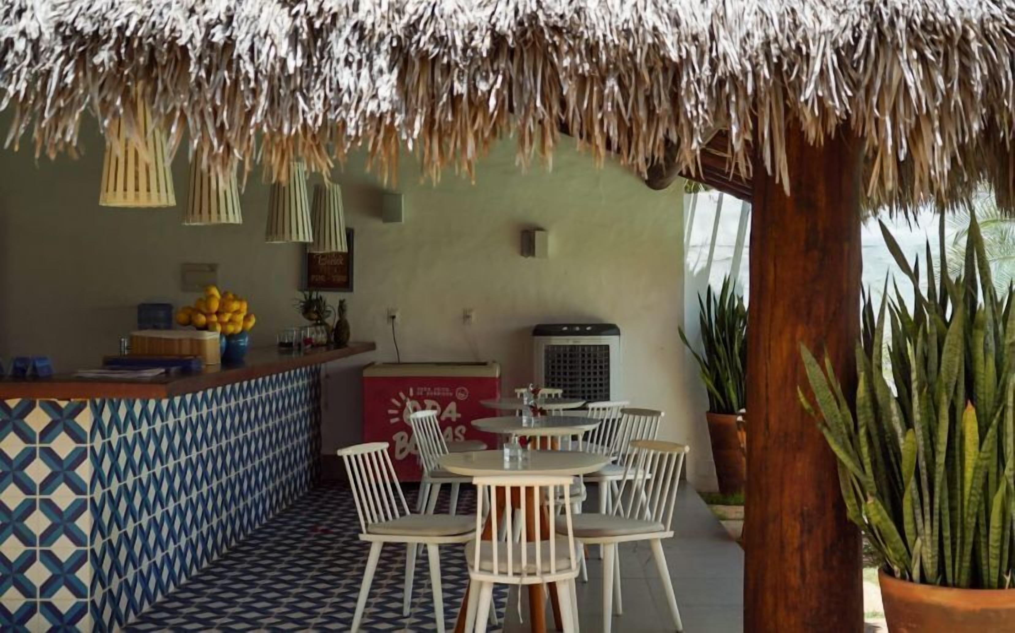 A restaurant with a thatched roof, outdoor seating, and a tiled floor.