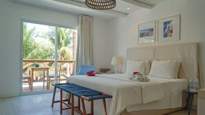 A bedroom with a large bed, a bench, a nightstand, and a view of palm trees through the balcony doors. - La Plage Hotel Boutique (Cajueiro da Praia)