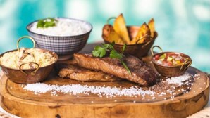 A wooden board with grilled fish, a bowl of rice, a bowl of salad, and a bowl of potatoes. - La Plage Hotel Boutique (Cajueiro da Praia)