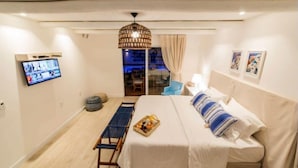 A hotel room with a bed, a TV mounted on the wall, a dining table with a basket of fruit, and a view of the outside balcony. - La Plage Hotel Boutique (Cajueiro da Praia)