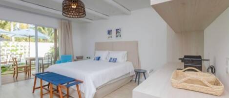 A modern bedroom with a bed, a small table, a chair, a hanging light fixture, and a view of the outdoors.