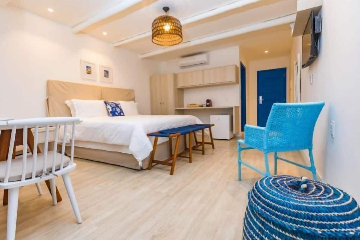 A bedroom with a bed, bedside table, and a chair. There is a desk and chair in the corner, and a TV mounted on the wall.